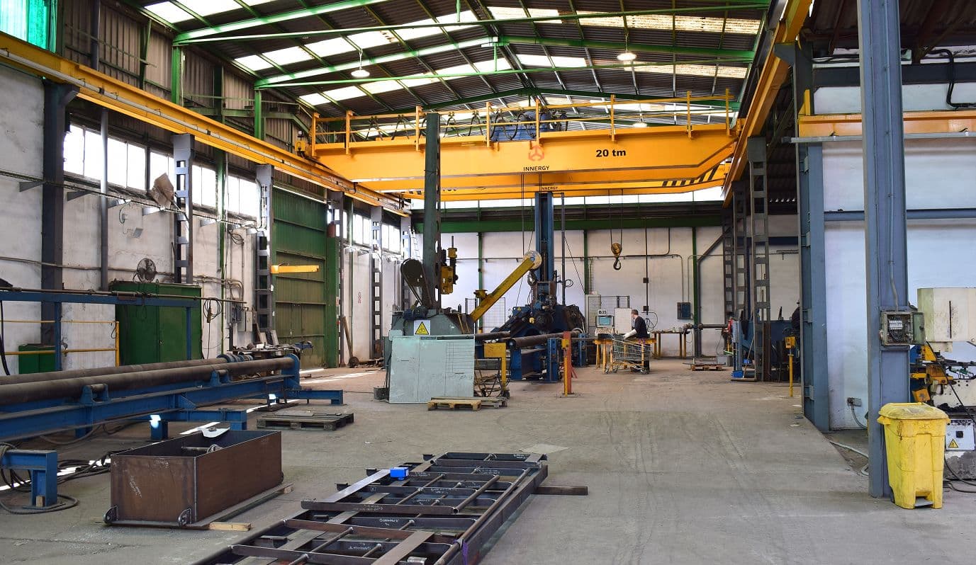 Interior de nave industrial con grúa puente amarilla de 20 toneladas, maquinaria pesada y postes metálicos”