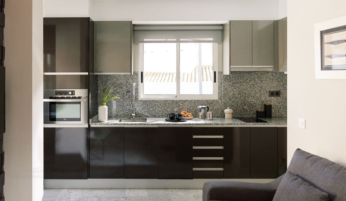 Cocina moderna con muebles oscuros, encimera de granito, fregadero bajo ventana y electrodomésticos integrados