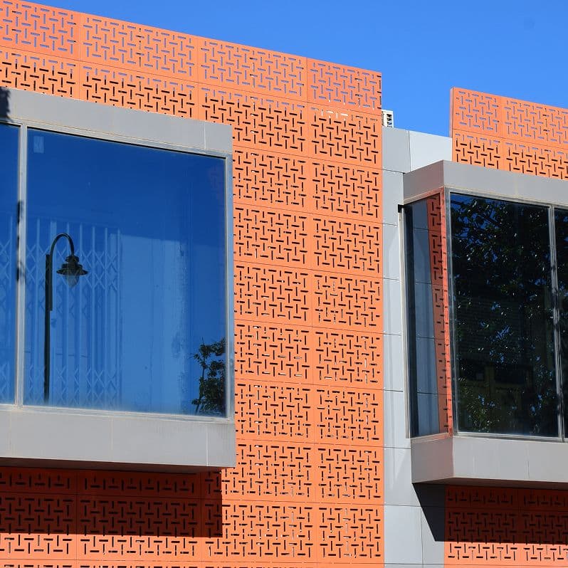 Fachada exterior de nave industrial con paneles perforados naranjas y amplias ventanas de cristal”